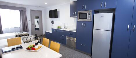 A modern hotel room with a dining area, a microwave, a refrigerator, and a flat-screen TV.