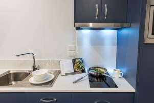 Cozinha moderna com pia de aço inoxidável, fogão por indução preto e luz azul embaixo dos armários.