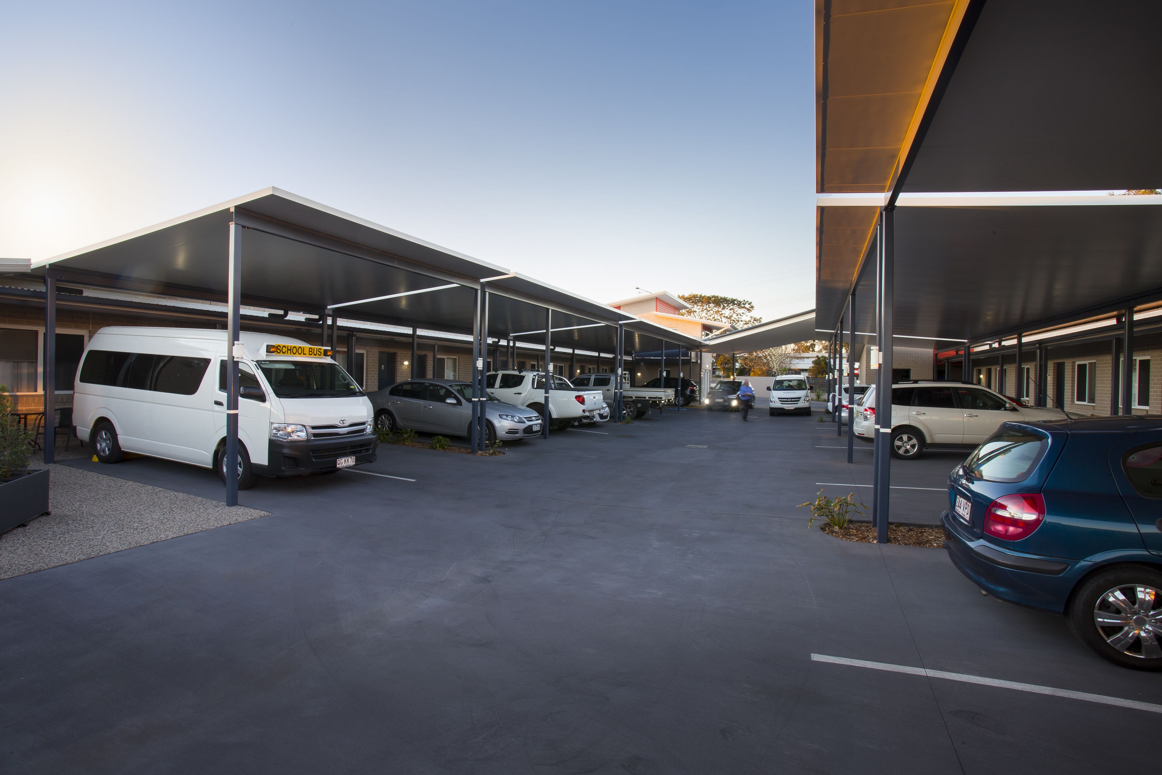A parking area with multiple vehicles, including a school bus, and covered structures.