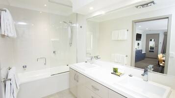 A modern bathroom with a large mirror, two sinks, a shower, and a bathtub.