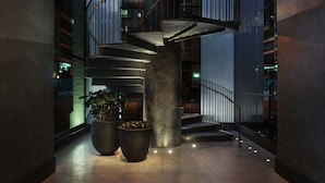 A modern interior with a spiral staircase, large potted plants, and a polished concrete floor. - 11 Howard, New York, a Member of Design Hotels (New York)