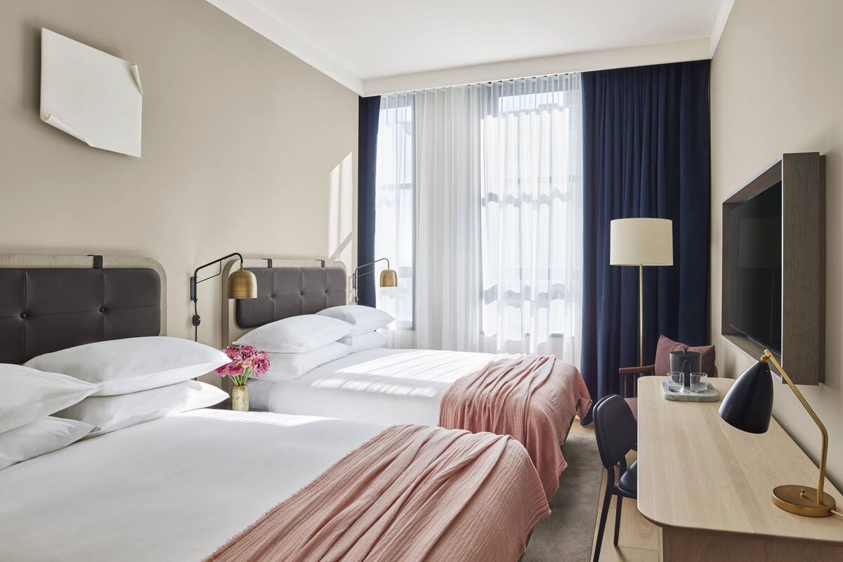 Hotelkamer met twee bedden, een bureau, een stoel, een televisie en een raam met gordijnen.
