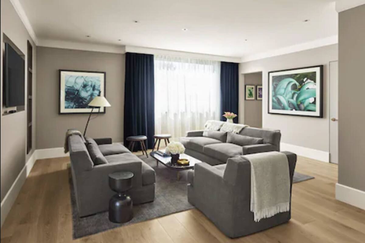 Een moderne woonkamer met twee grijze banken, een salontafel en een vloerlamp. Er hangen twee ingelijste kunstwerken aan de muur en een raam met gordijnen.