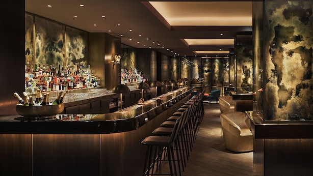 A bar area with a long counter, stools, and a wall of liquor bottles. - 11 Howard, New York, a Member of Design Hotels (New York)