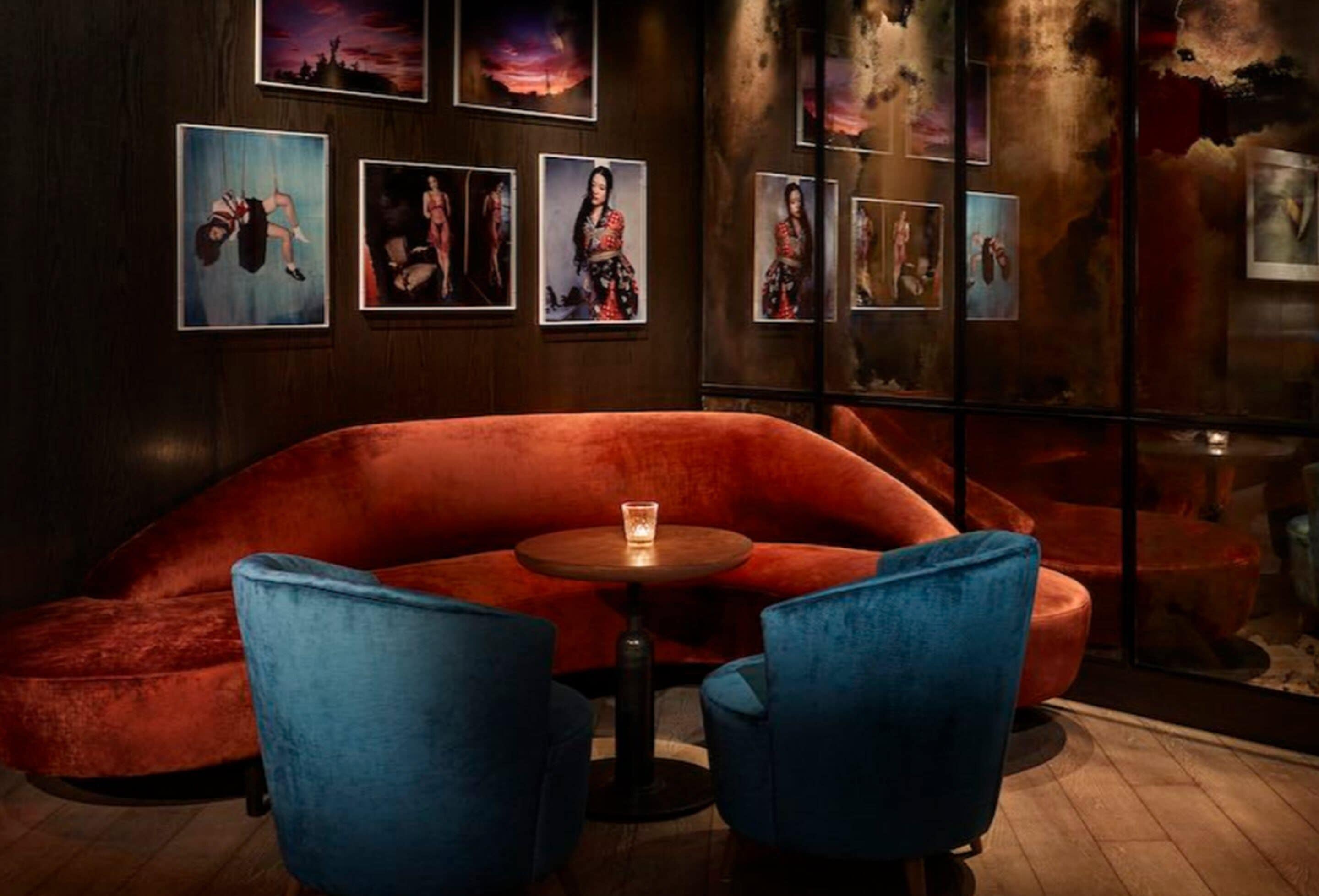 A room with a red velvet sofa, two blue armchairs, and a small round table with a candle.