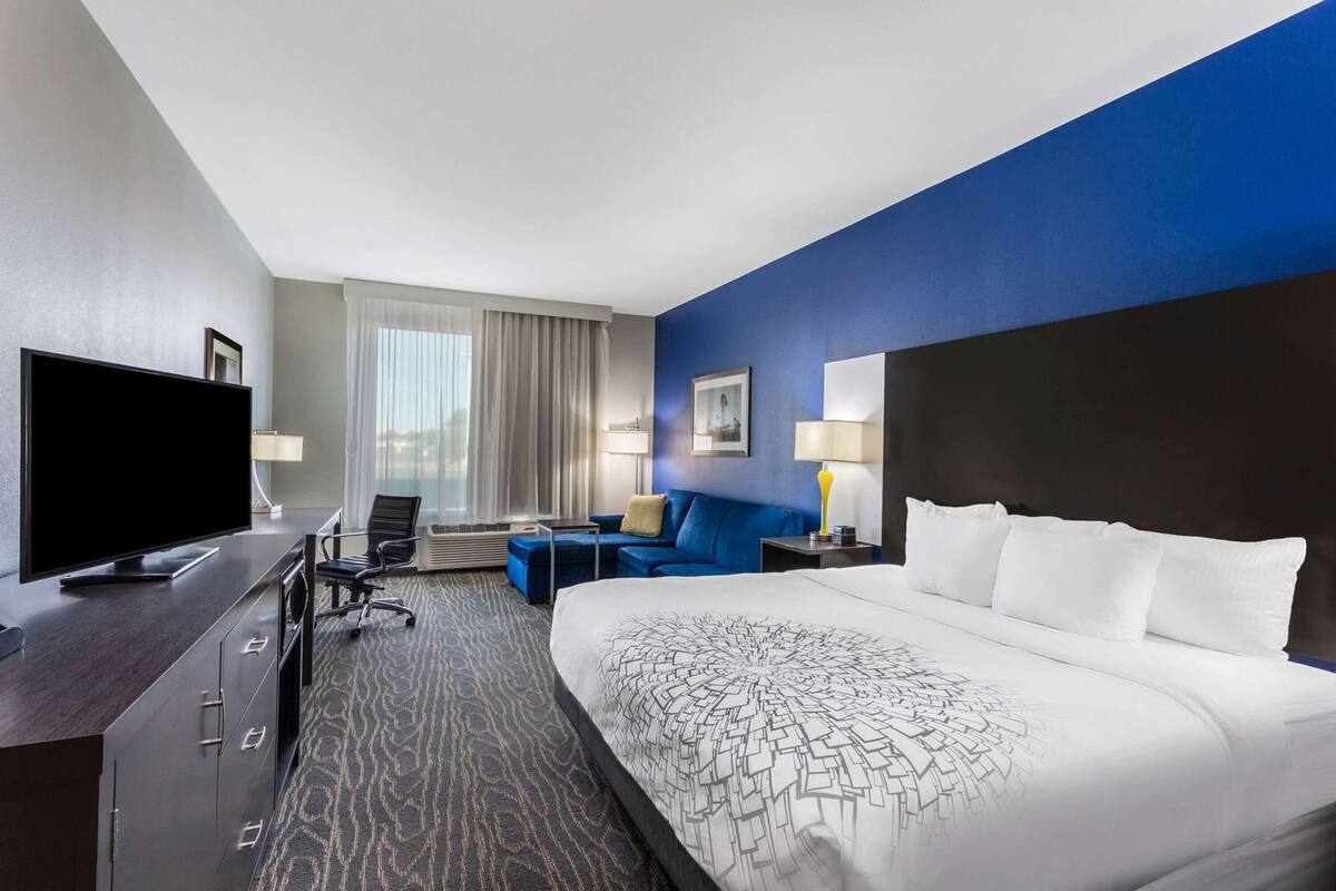 Habitación de hotel con una cama grande, televisión de pantalla plana, escritorio con silla, sofá y ventana con cortinas.