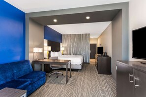 A hotel room with a bed, a desk, a blue sofa, a TV, and a wardrobe.
