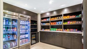 Un bar de aperitivos bien iluminado con dispensadores de bebidas refrigeradas y estantes llenos de diferentes bocadillos y productos envasados.