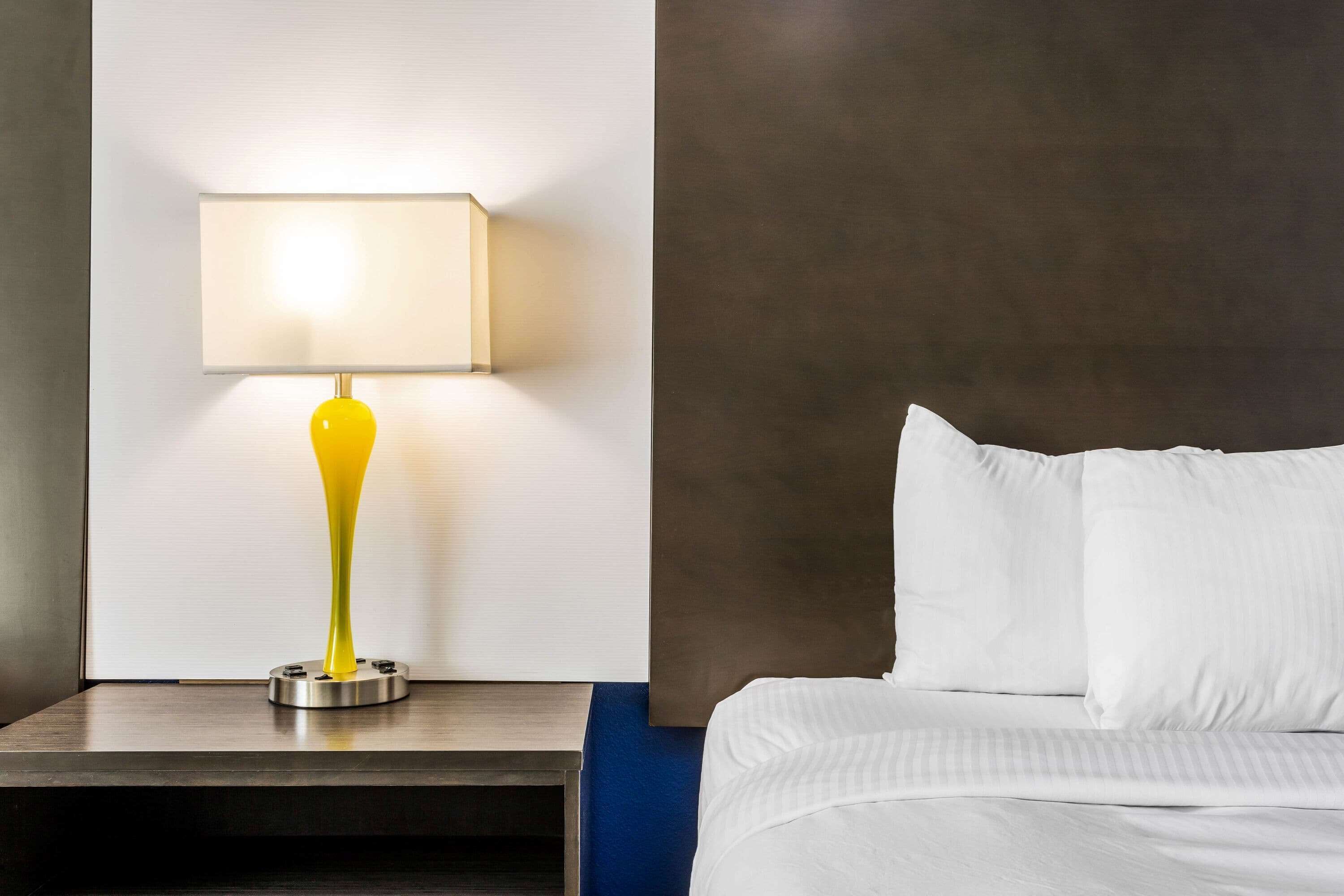 A hotel room with a bed, a nightstand, and a lamp.