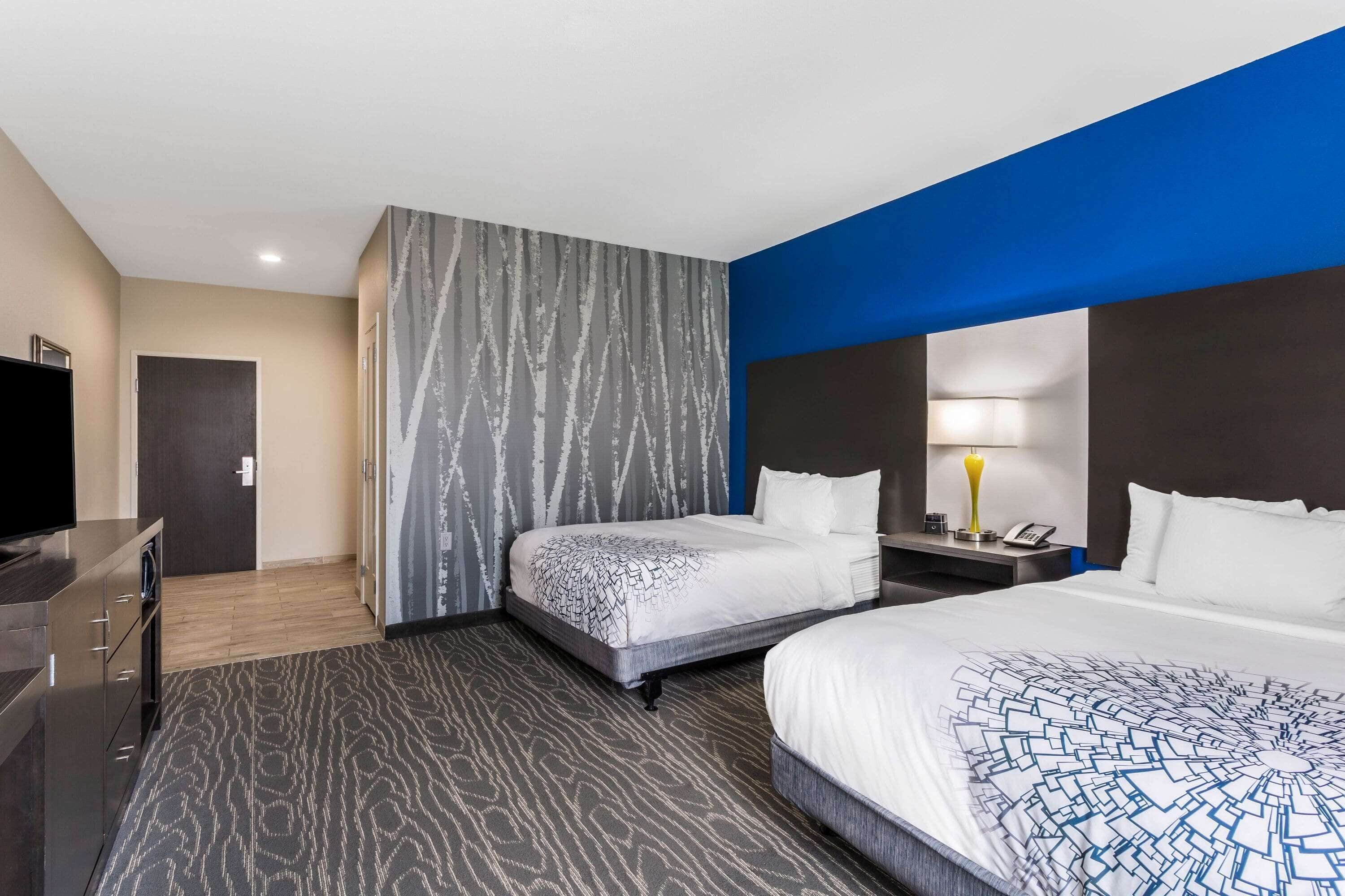 Ein Hotelzimmer mit zwei Betten, einem Fernseher, einem Schreibtisch und einer Lampe.
