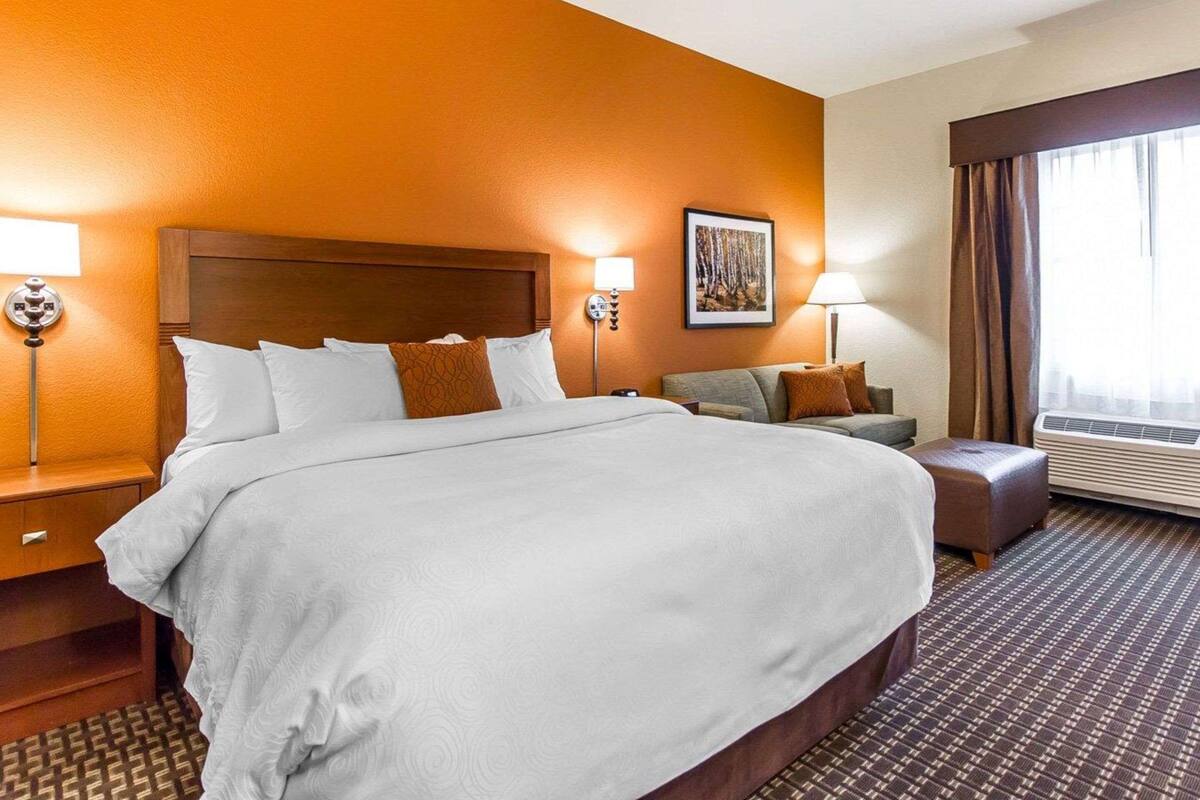 A hotel room with a large bed, a sofa, a desk, and a window with curtains.