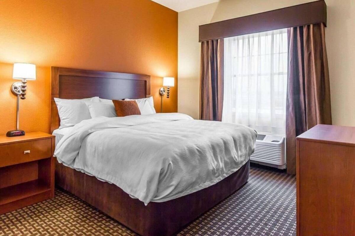 A hotel room with a large bed, bedside lamps, a nightstand, a desk, and a window with curtains.