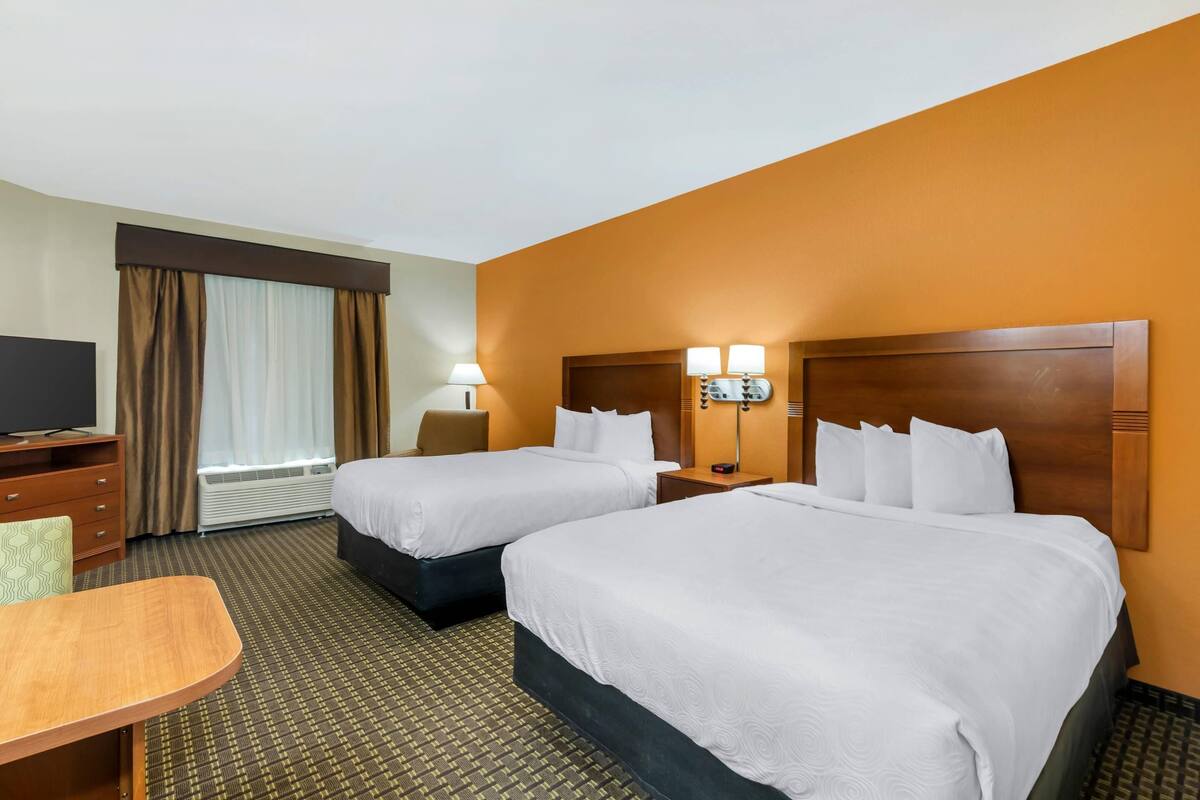 A hotel room with two beds, a desk, a chair, a TV, and a window with curtains.