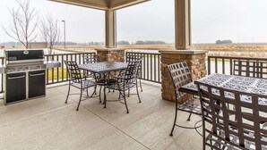A covered patio with a grill, outdoor table, and chairs, overlooking a field. - MainStay Suites Stanley (Stanley)