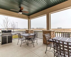 Un patio cubierto con una parrilla, una mesa y sillas al aire libre, con vista a un campo.