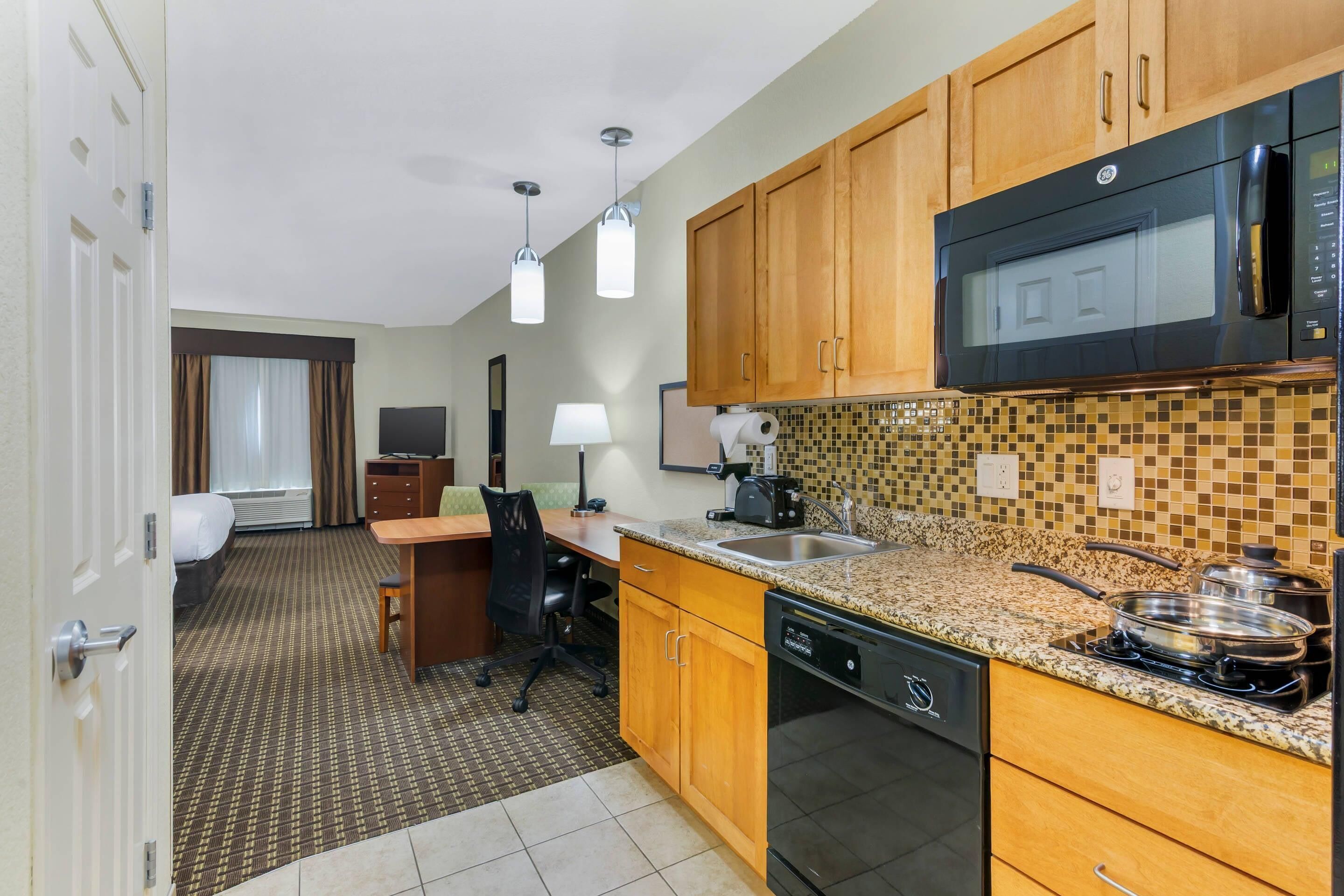 A compact kitchen with wooden cabinets, a microwave, a dishwasher, and a granite countertop.