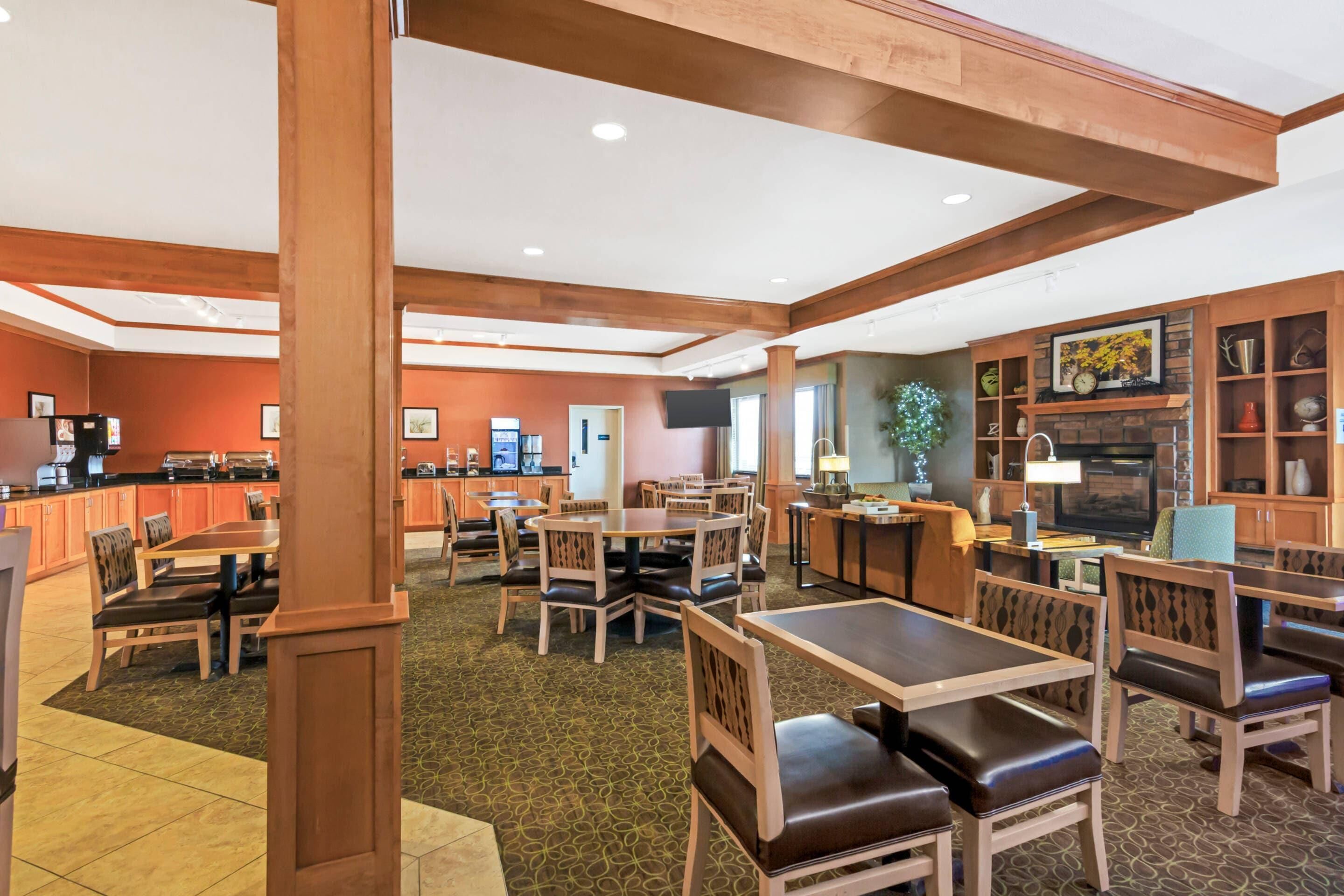 A hotel lobby with wooden furniture, a kitchen area, and a seating area with tables and chairs.