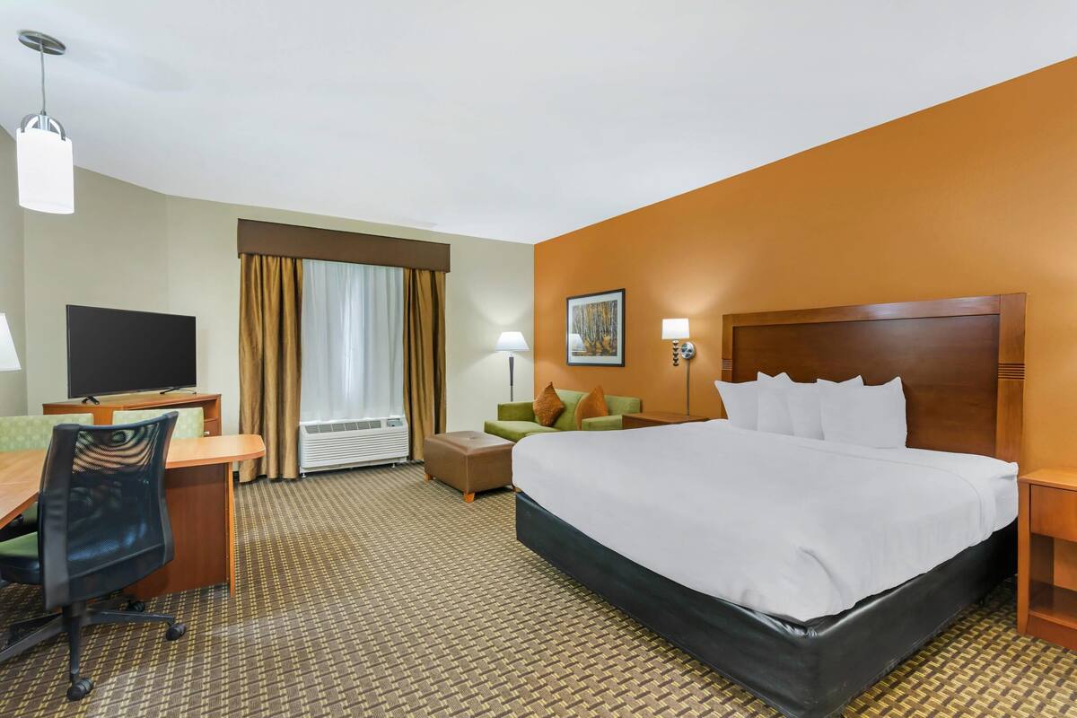 A hotel room with a large bed, a desk with a chair, a television, and a window with curtains.