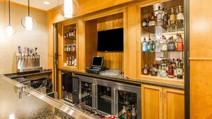 A bar area with a long counter, a television screen, and shelves stocked with various liquor bottles. - MainStay Suites Stanley (Stanley)