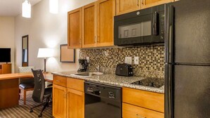 A compact kitchen with wooden cabinets, a black microwave, a refrigerator, a toaster, and a dishwasher. - MainStay Suites Stanley (Stanley)