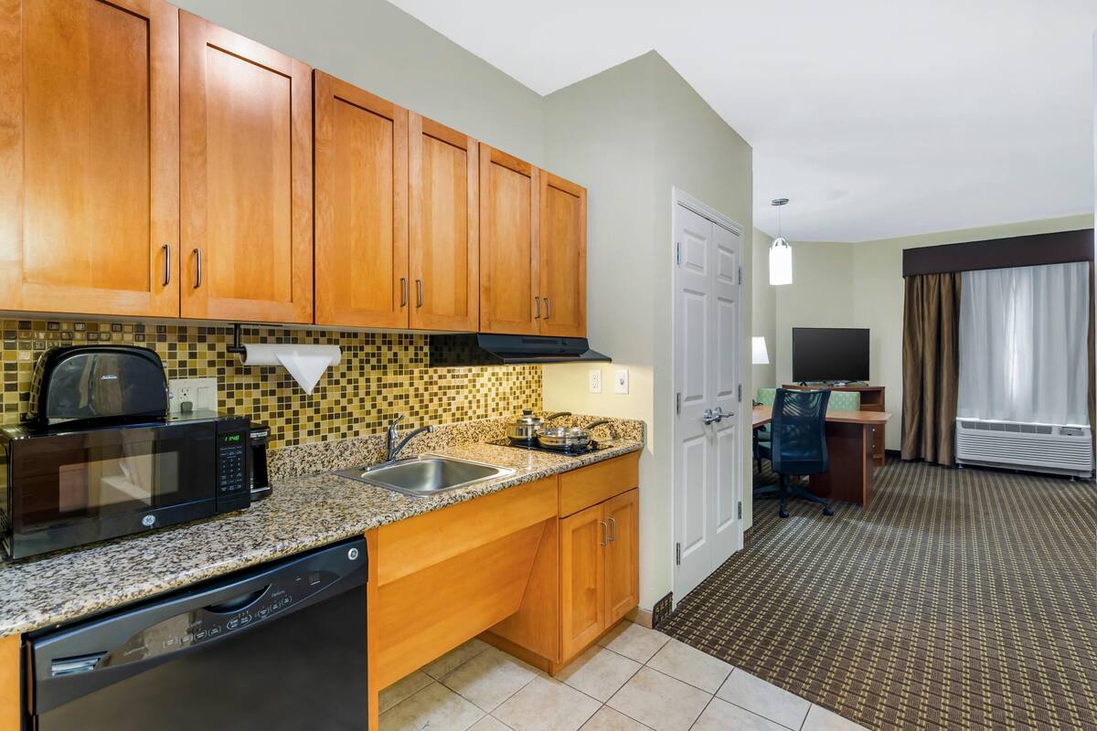A compact kitchen with wooden cabinets, a microwave, a dishwasher, and a tiled backsplash.