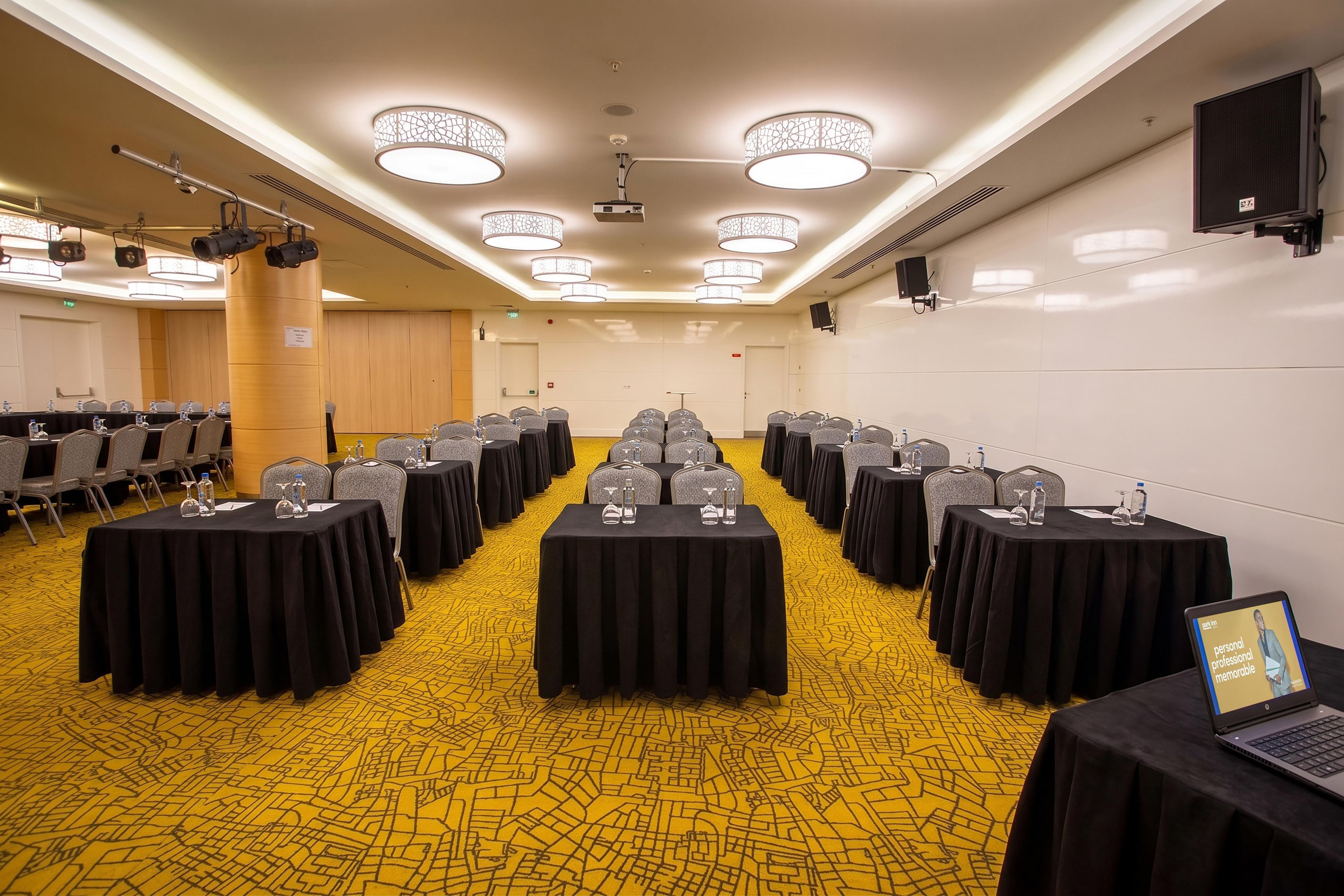 A conference room with rows of tables, chairs, and a yellow patterned carpet.