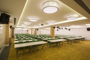 Un salón de conferencias con varias mesas y sillas, iluminación en el techo y suelo alfombrado.