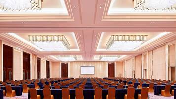 A conference room with rows of tables and chairs, a large screen at the front, and a chandelier.