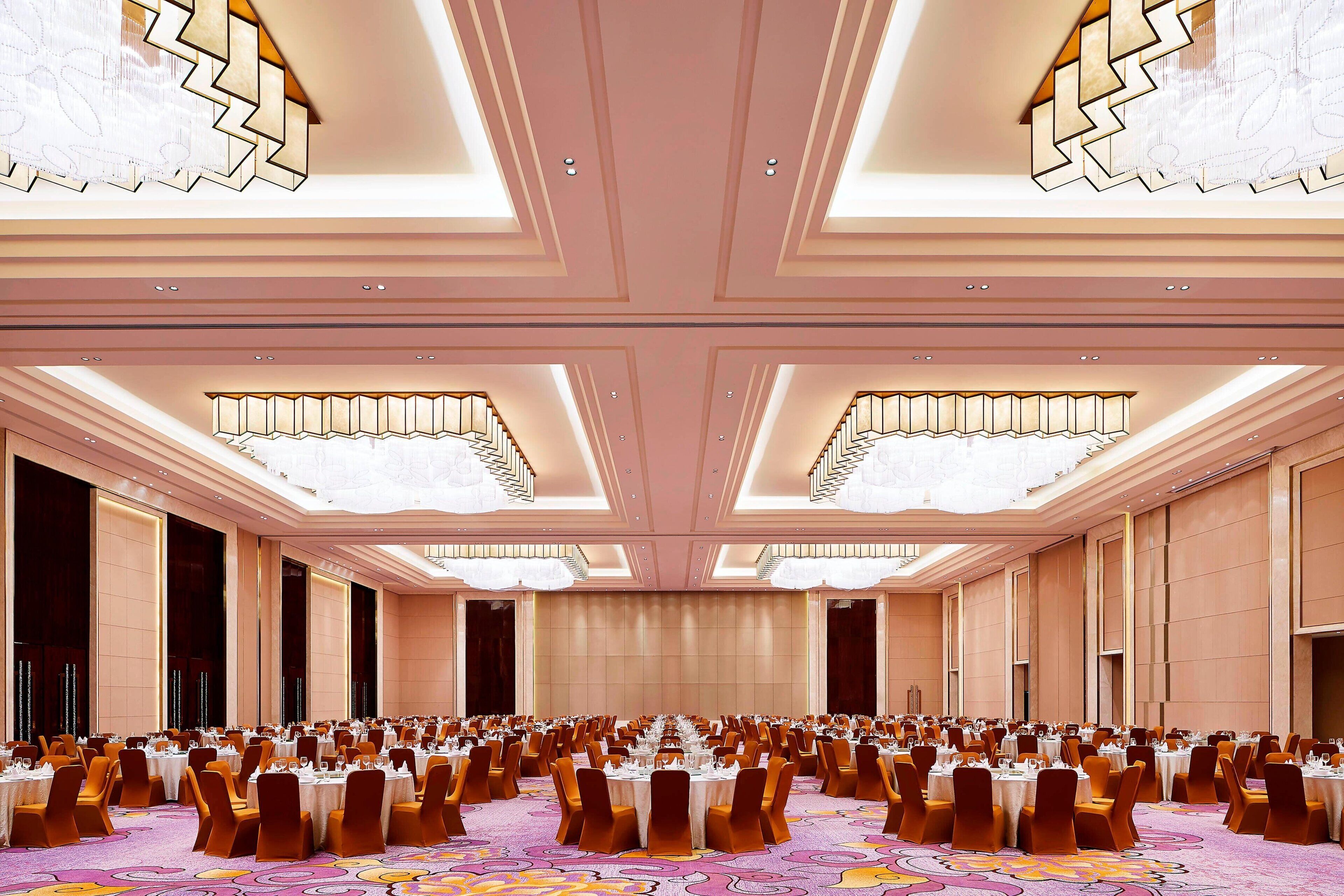 Un amplio salón de banquetes con filas de mesas dispuestas para comer, techos altos con candelabros y una alfombra estampada.