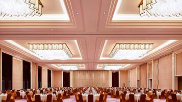 Un amplio salón de banquetes con filas de mesas dispuestas para comer, techos altos con candelabros y una alfombra estampada.