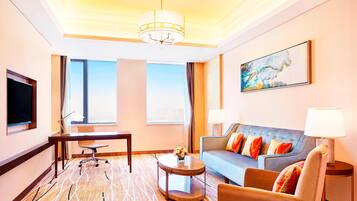 A hotel room with a large window, a sofa, a desk, and a television.