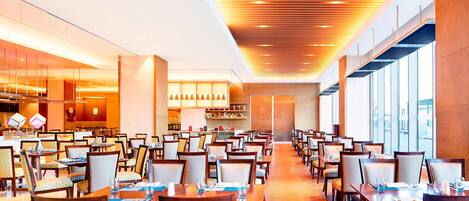 Un comedor amplio con varias mesas y sillas, un diseño de techo moderno y grandes ventanales que ofrecen luz natural.