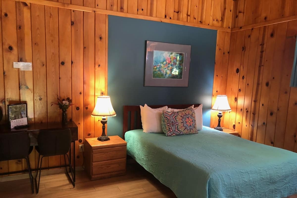 A room with a bed, two bedside tables with lamps, a desk with a chair, and a framed picture on the wall.