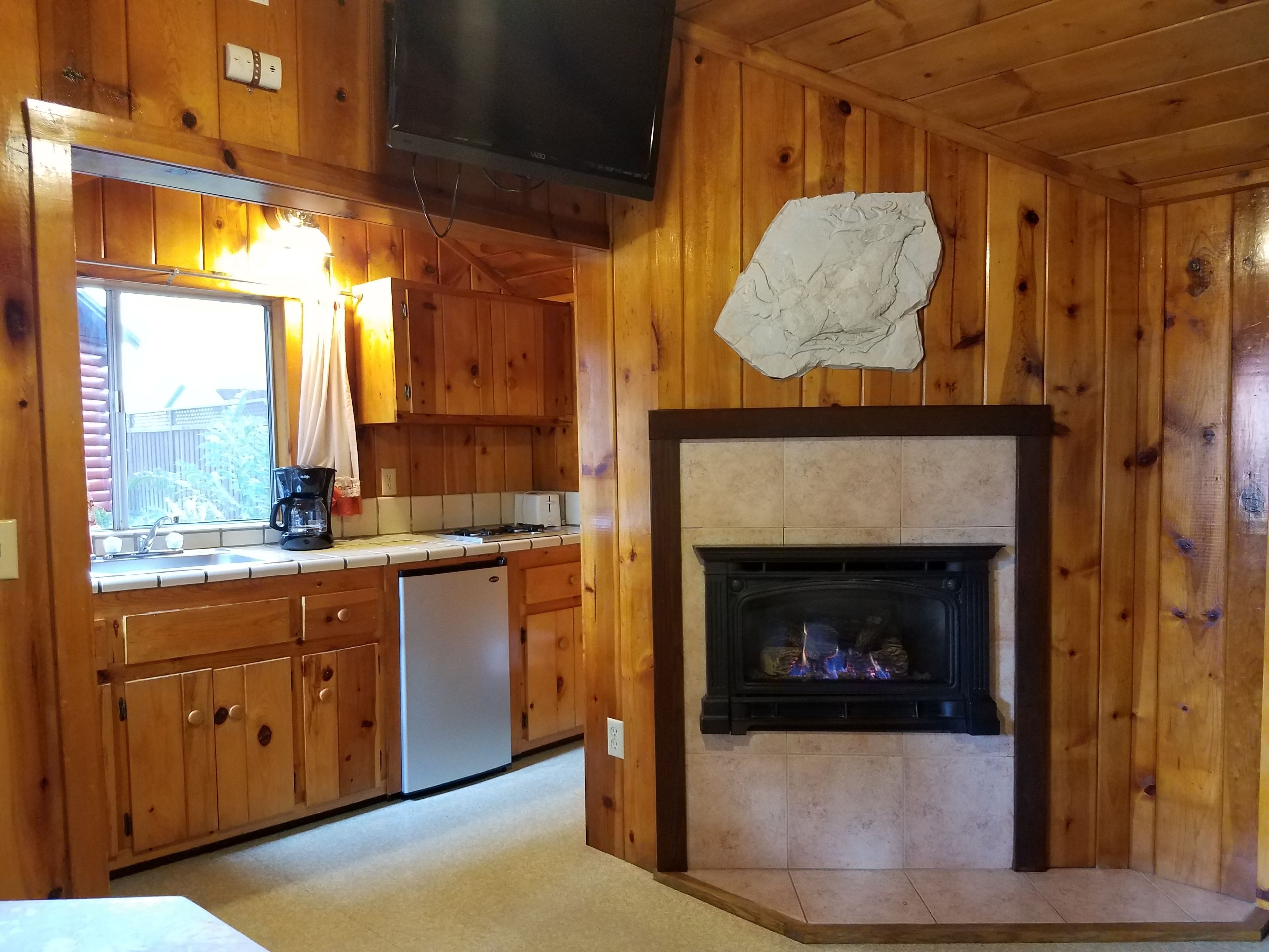 A wooden cabin interior with a kitchen area, a fireplace, and a television mounted on the wall.