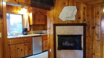 A wooden cabin interior with a kitchen area, a fireplace, and a television mounted on the wall.