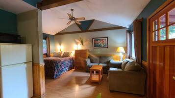 Um quarto aconchegante com uma cama, dois sofás, uma mesa de madeira, um ventilador de teto e uma janela com cortinas.