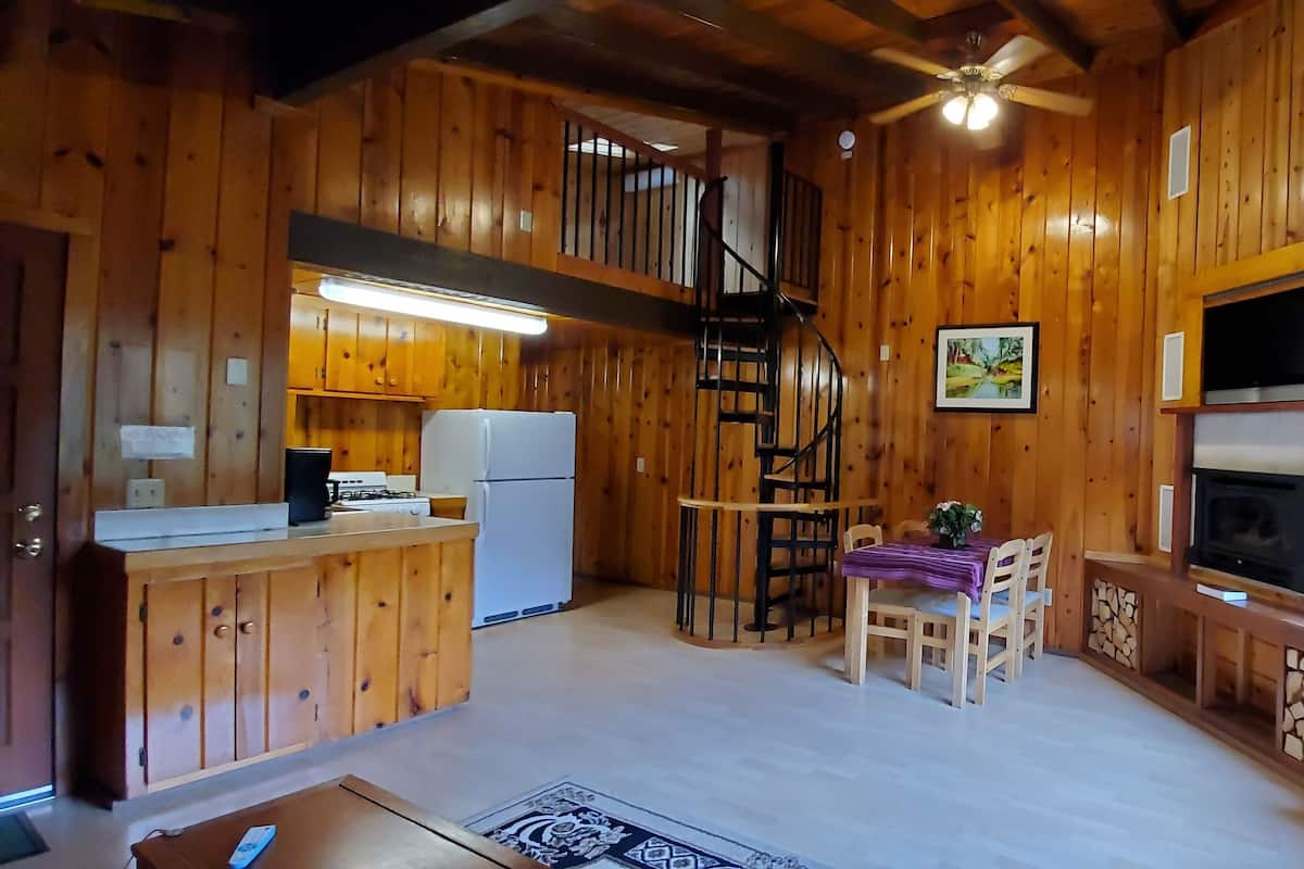 A wooden cabin interior with a kitchen, dining area, and a fireplace.