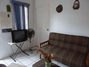 En stue med fjernsyn, ventilator, sofa og en dekorativ vase.