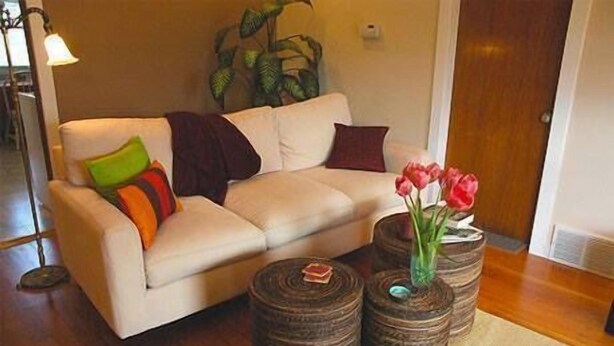 Een woonkamer met een beige bank, kleurrijke kussens en een vaas met rode bloemen op een ronde houten tafel.