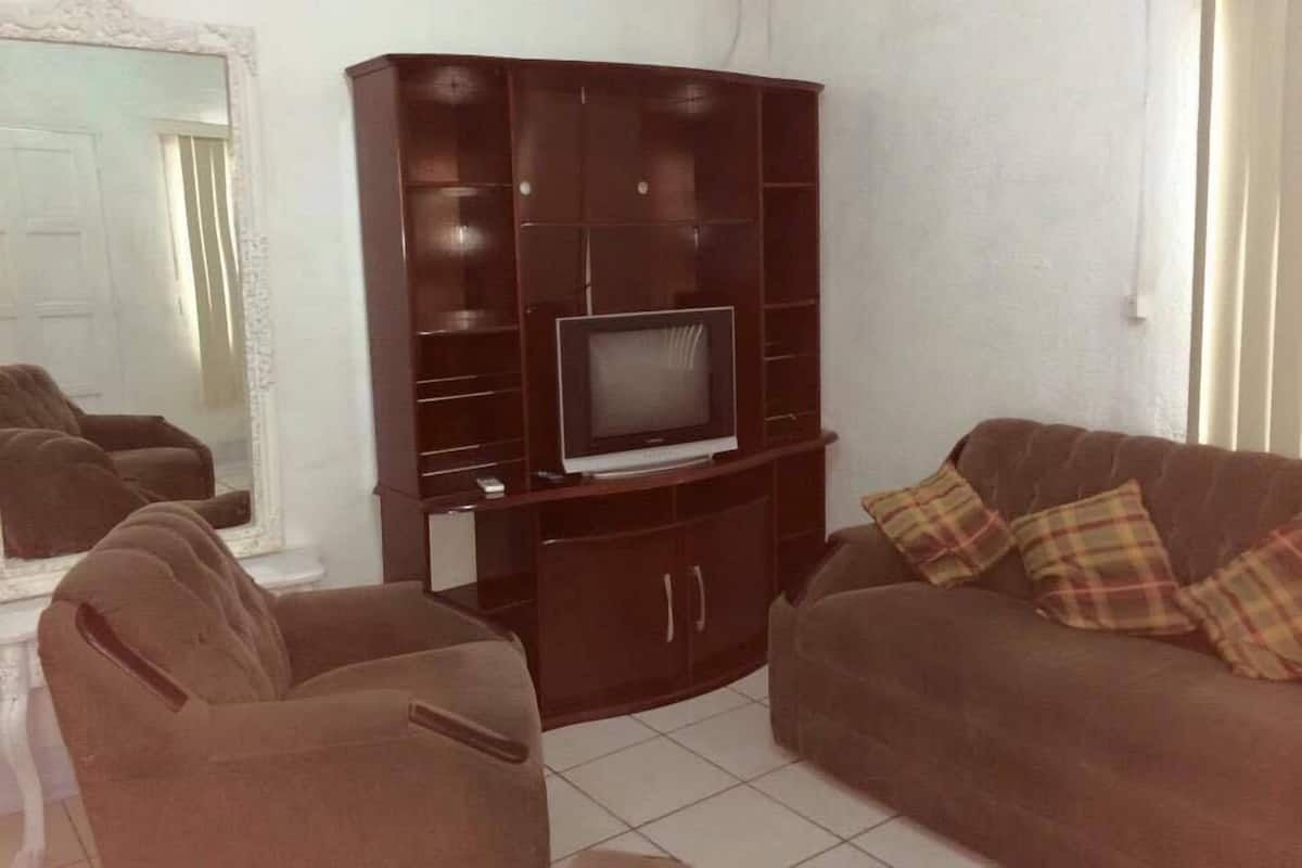 Un soggiorno con un mobile TV in legno scuro, una televisione, due divani marroni e uno specchio.