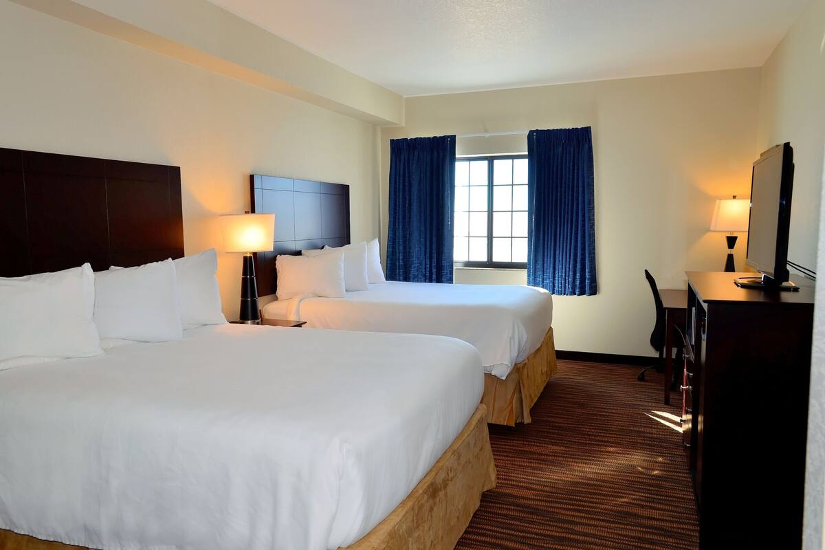 A hotel room with two beds, a desk, a chair, a TV, and a window with curtains.