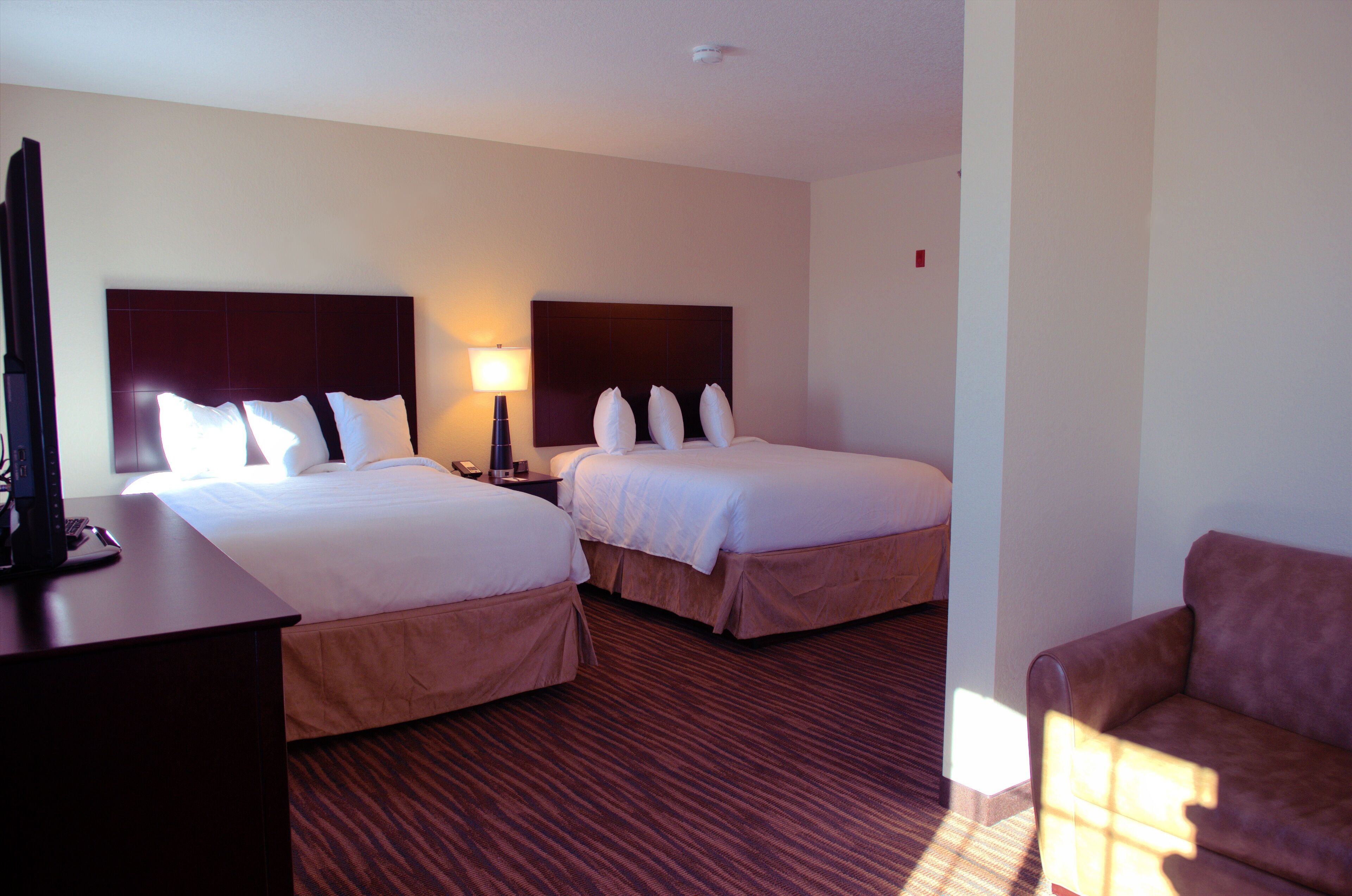 A hotel room with two beds, a desk with a lamp, and a sofa.