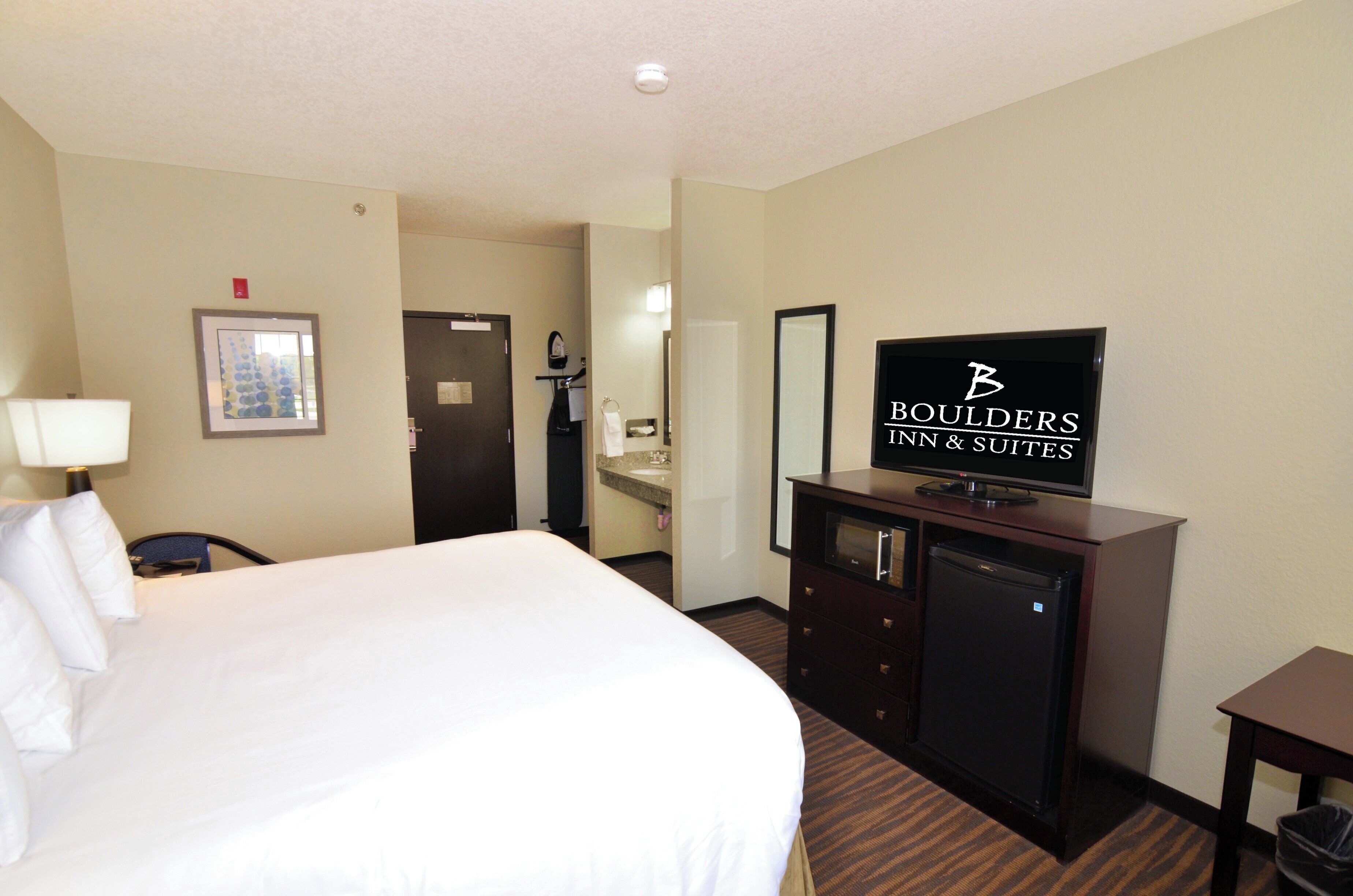 Ein Hotelzimmer mit einem großen Bett, einem Fernseher, einem Schreibtisch und einem durchgegangenen Badezimmer.