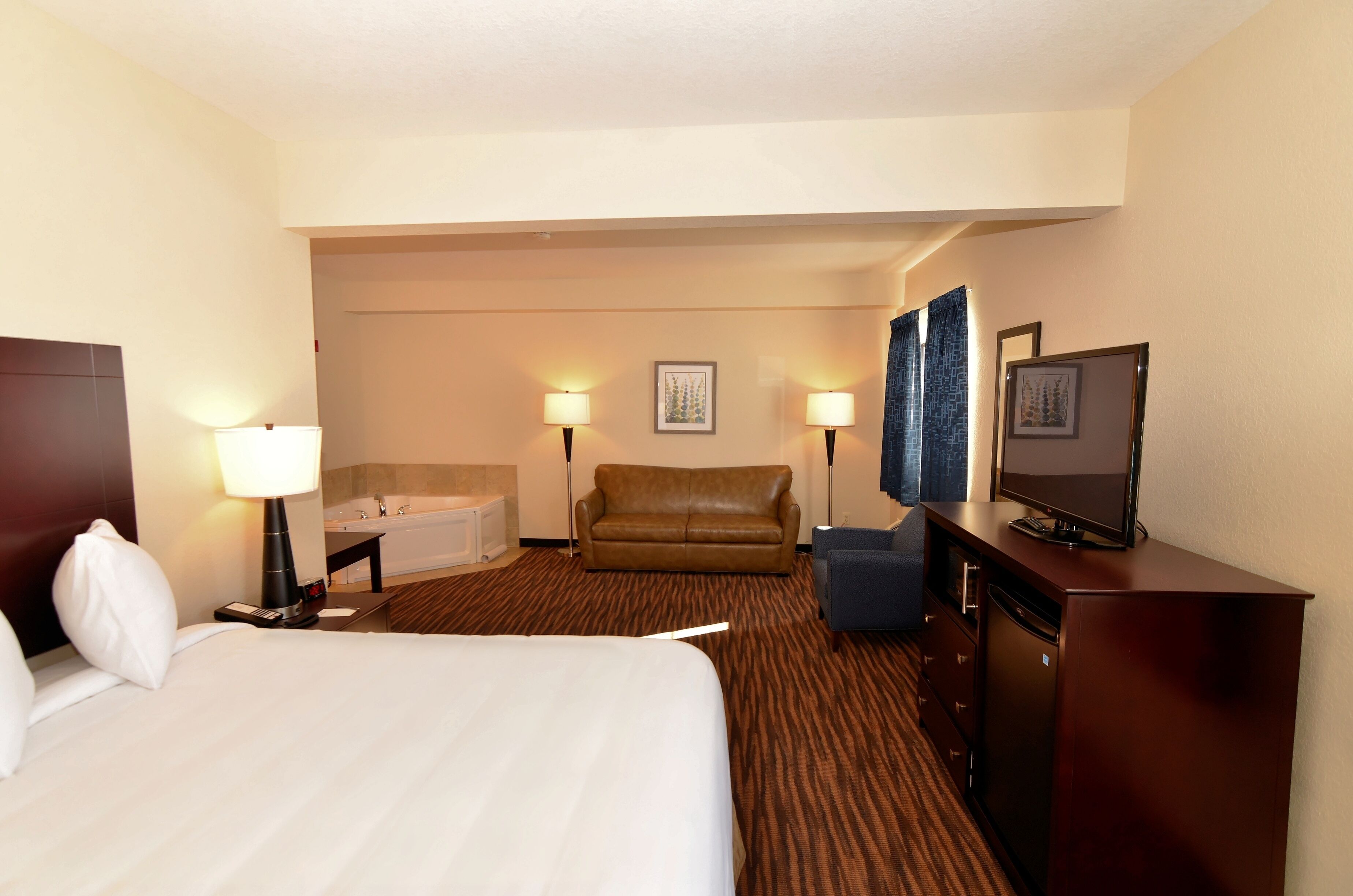 A hotel room with a bed, a sofa, a desk with a television, a lamp, a picture frame, and a bathroom with a bathtub.