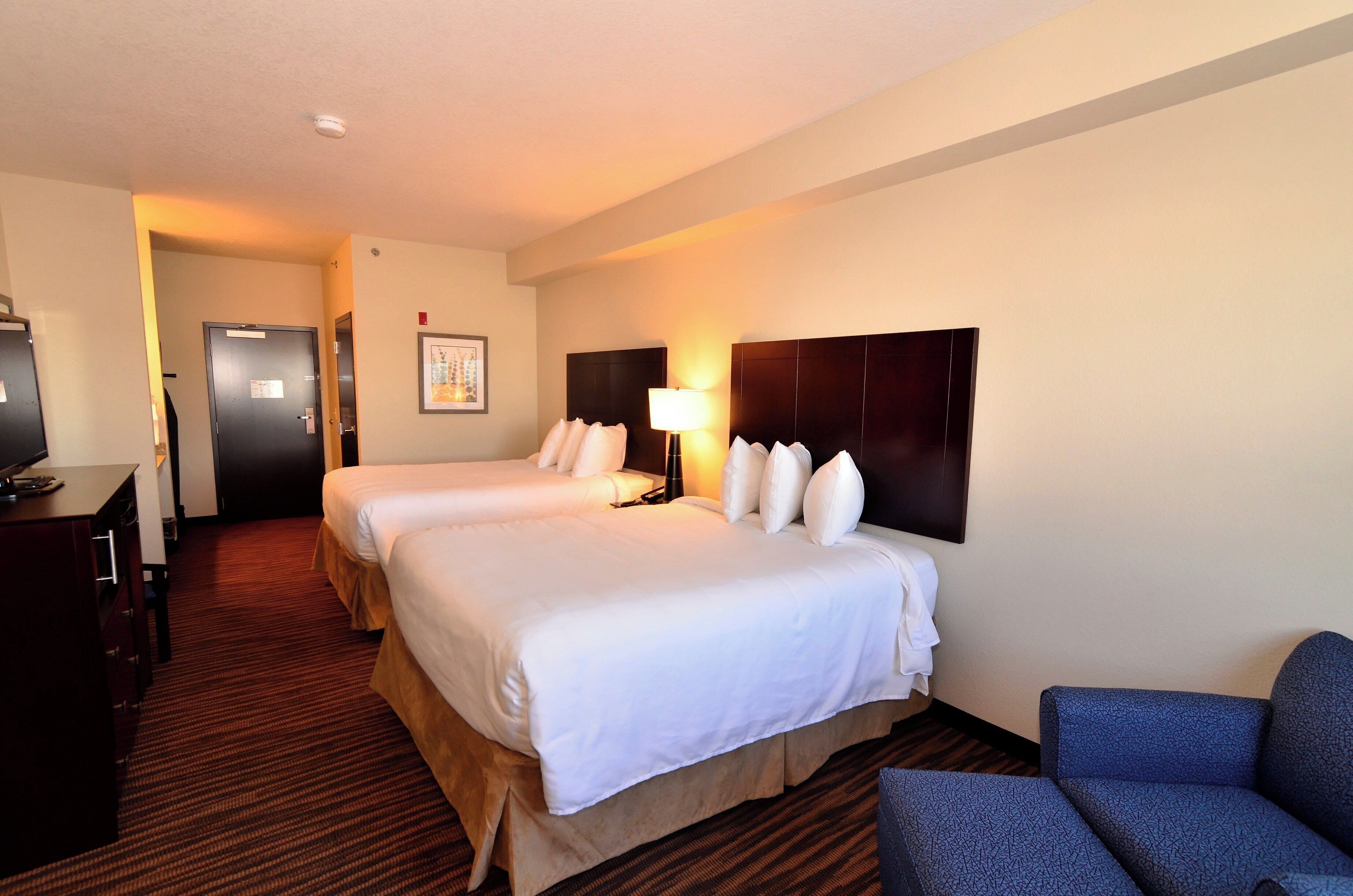 A hotel room with two beds, a desk, a chair, and a wall-mounted TV.