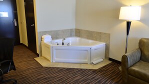 Habitación de hotel con una bañera blanca, un escritorio con silla, una lámpara y una puerta.