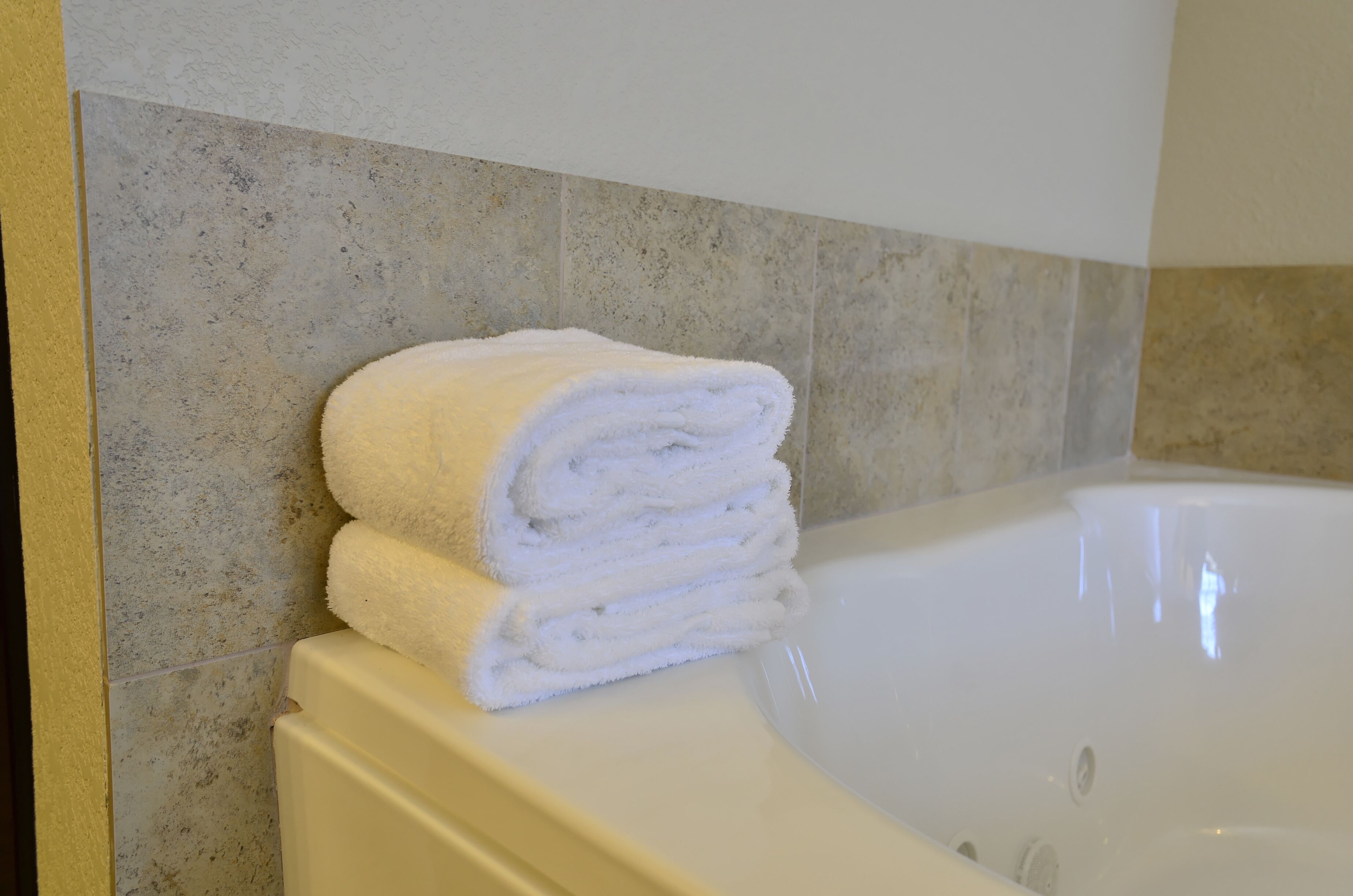Un baño con una bañera blanca y una pila de toallas blancas en el borde.