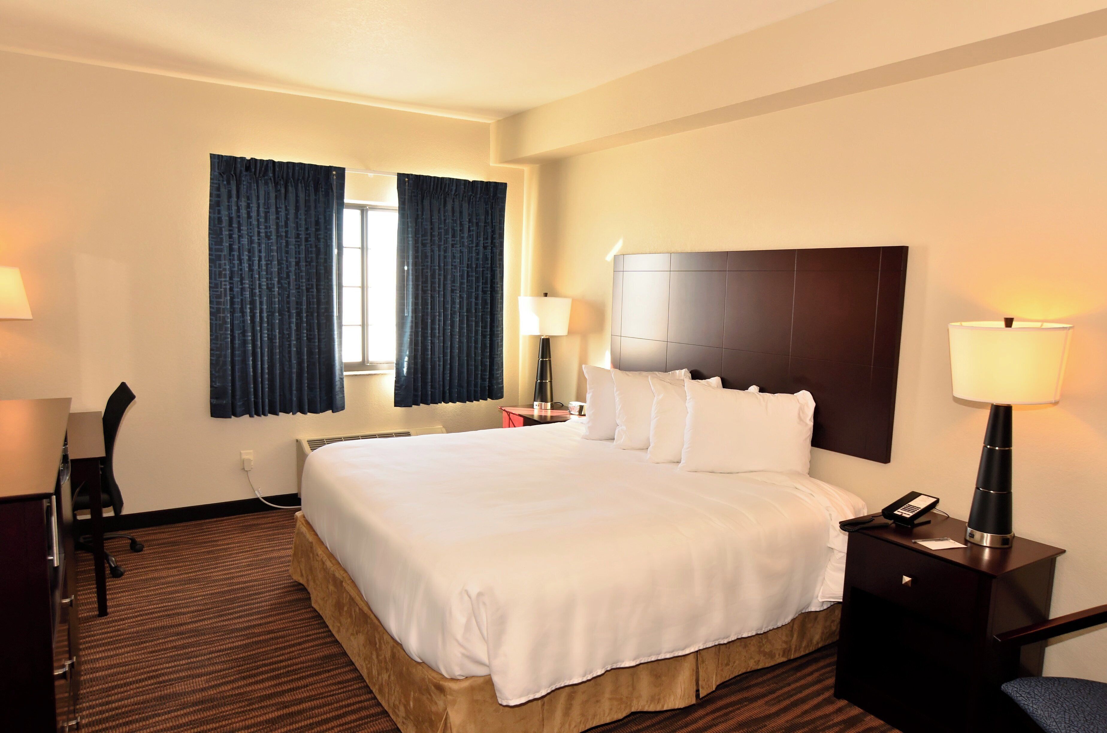 Une chambre d’hôtel avec un grand lit, deux tables de chevet avec des lampes, un bureau et une chaise.
