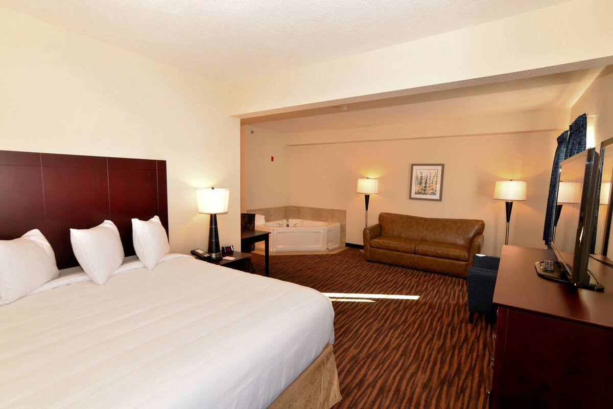 A hotel room with a large bed, a sitting area with a sofa, a desk, and a bathtub.