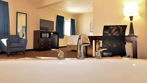 Habitación de hotel con una cama grande, un escritorio con ordenador, una silla, un televisor y un baño con lavabo y espejo.